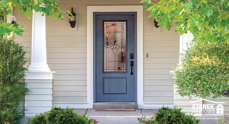 Colonial blue entry door with decorative glass and black hardware on tan home with white wood pillars.
