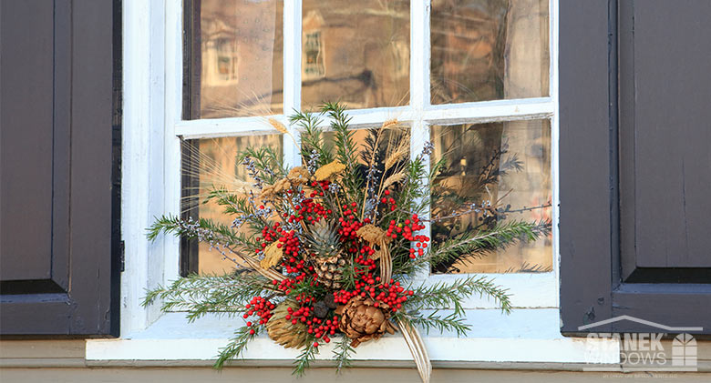 Elegant holiday display on a window with evergreens, pinecones, dried flowers and grasses, red berries, and white twigs.