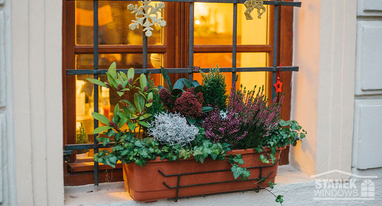 Holiday window box decorated with live plants and flowers, as well as dried flowers and twigs in red, green, and white.