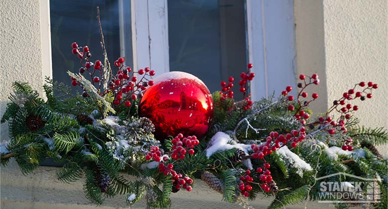 A window ledge decorated with evergreen branches and red berries, a large red ornament in the center.