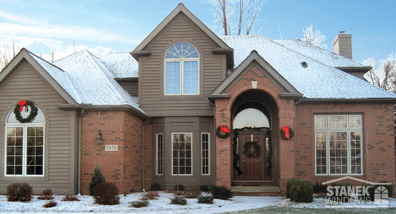 The exterior of a home decorated for the holidays with garland and wreaths with red bows. A dusting of snow on the ground.