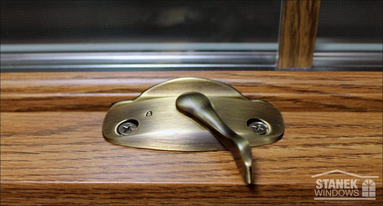 A closeup of a lock on a woodgrain vinyl window.