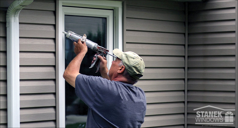 A man caulking a window from the outside.