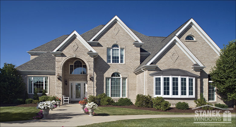 A beautiful gray brick home with arched entryway, stylish windows, including a bay, & surrounded by a nicely landscaped yard.