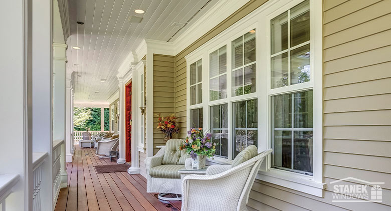 A row of single-hung windows with a half screen viewed from the porch of a tan home.