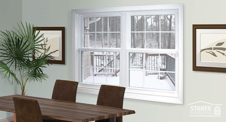 White double-hung windows with colonial grids in a dining room with a plant in the corner and art prints on the wall.